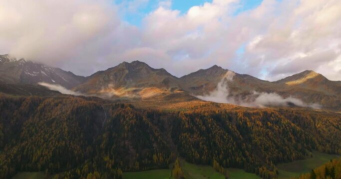 Glowing golden Casere mountain with misty low cloud over autumn alpine valley forest trees