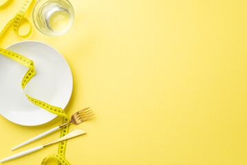 Weight loss concept. Top view photo of plate glass of water measuring tape knife and fork on...
