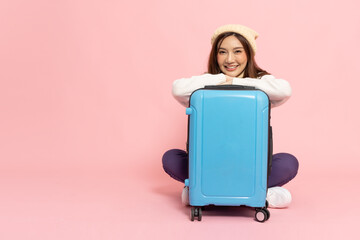 Happy Asian woman traveler sitting on floor with luggage isolated on pink background, Tourist girl...
