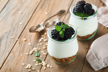 Fototapeta na wymiar Yogurt with granola, blackberry berry fruits and muesli served in glass jar on wooden background. Healthy breakfast concept. Healthy food for breakfast, top view
