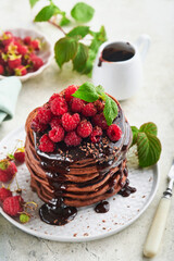 Chocolate Pancakes. Pancakes with fresh raspberry with chocolate glaze or toppings in gray bowl on light gray table background. Homemade classic american pancakes. Page for magazine concept.