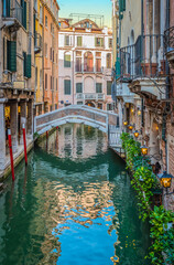 Narrow canal with small bridge and romantic lights on beautiful Venetian buildings in city center of Venice, Italy. 