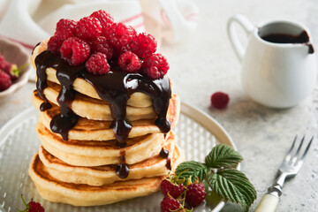 American pancakes. Stack pancakes with fresh raspberry with chocolate glaze or toppings in white bowl on light gray table background. Homemade classic american pancakes. Magazine concept. Top view.