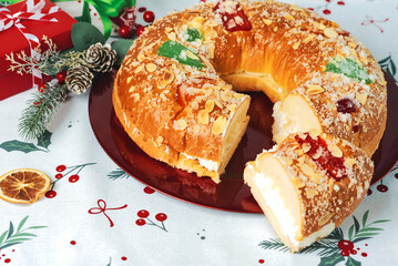 Roscon de reyes with cream and christmas ornaments on a red plate. Kings day concept spanish three...