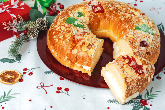 Roscon de reyes with cream and christmas ornaments on a red plate. Kings day concept spanish three kings cake.Typical spanish dessert for Christmas
