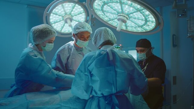 Four medical surgeons are in a room filled with different medical equipment working on a patient and standing around him.