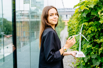 Portrait of young female student with turbine model on modern building terrace with green garden....