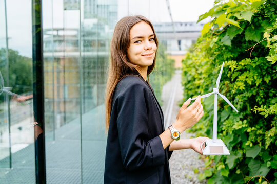 Portrait of young female student with turbine model on modern building terrace with green garden. Project presentation work.