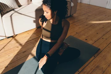 Foto op Plexiglas Top view of pretty pregnant african american girl in sports clothes doing twits sitting in lotus posture on floor, under sun rays, practicing prenatal yoga, preparing body for childbirth © shurkin_son
