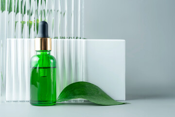 Green glass cosmetic bottle with pipette next to white podium and glass window, product packaging with natural ruscus branch, anti aging serum with peptides, cosmetics mockup, spa concept.