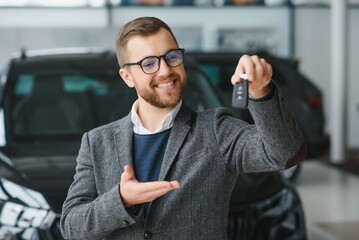 Good looking, cheerful and friendly salesman poses in a car salon or showroom.