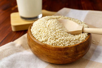 Sesame milk in a glass, raw seeds, wooden background. Dairy free alternative