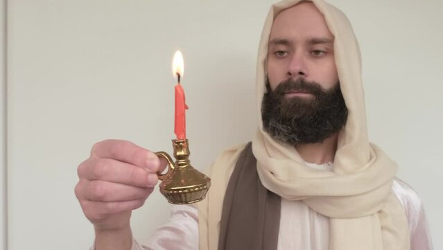 biblical scene, Jesus Christ Hand holds burning candle, young bearded and mustachioed man in image of Savior, selective focus on hand with candle, concept Holy Scriptures, symbol Christian religion