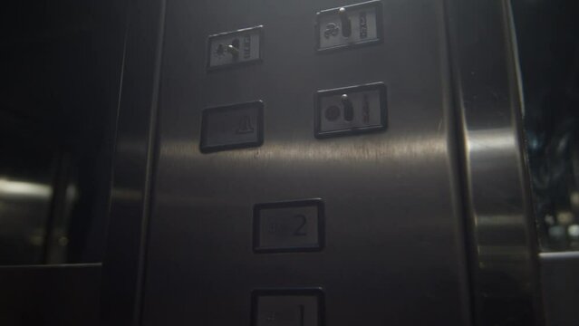 closeup of the hand of a man inside a metallic elevator pressing the button for the second floor in slow motion