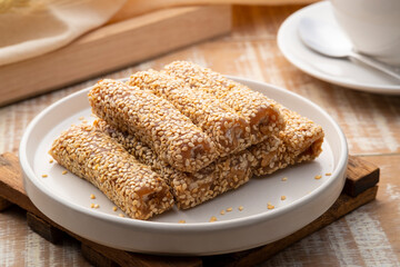 Golden brown roasted sesame seeds and peanuts are bound together by sugar to form delicious sesame bars,Thai snacks,Sesame Roll on white plate