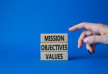Mission Objectives Values symbol. Concept words Mission Objectives Values on wooden blocks. Beautiful blue background. Businessman hand. Business and Mission Objectives Values concept. Copy space