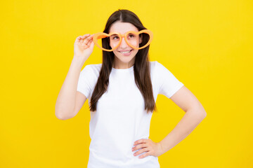 Girl with heart shaped glasses funny and smiling on yellow studio background.