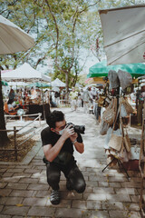 Smart young man traveller knees sitting and using his camera take a photo in street market