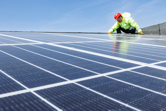 operaio con caschetto protettivo rosso , tuta specialistica e occhiali tecnici lavora su un impianto fotovoltaico istallato sul tetto di un edificio