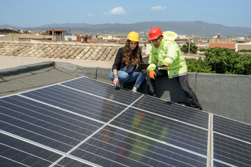 un ingegnere con l'operaio controllano la posa in opera dei pannelli fotovoltaici nel tetto di un...