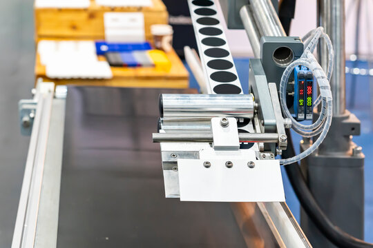 Close up automatic continuous labeling machine for labelling product on belt conveyor in manufacturing process in industrial