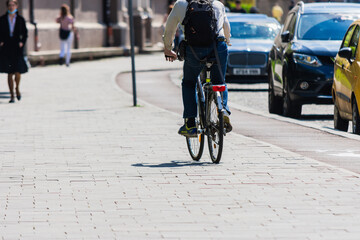 Unrecognizable man riding a bike in city with blurred people and cars in background in hard sunlight