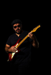 Man playing electric guitar wearing a flat cap and sunglasses.