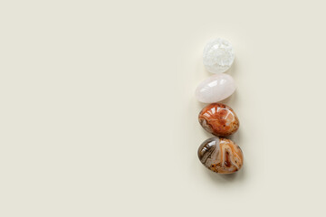 Aesthetic minimal flat lay with pebble stones on beige color background with copy space. Row from natural smooth stone, sardonyx and pink quartz gemstone. Summer concept, top view