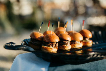 A platter of beef sliders on a table outside for an event

