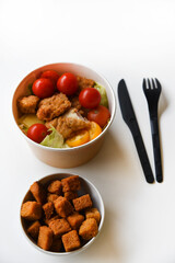 Caesar salad with tomatoes and breadcrumbs in containers. Delicious breakfast with accessories on a white background. Salad with meat and breadcrumbs.