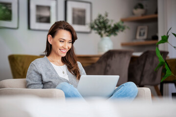 Smiling caucasian woman using laptop while sitting in an armchair at home