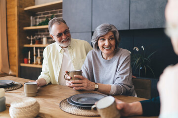 Cheerful couple drinking hot beverages while talking to anonymous friends