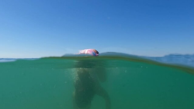 Half underwater scene of young redhead girl doing handstand in seawater with horizon in background. Slow motion summer holiday concept