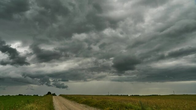 A timelapse storm over a field and a dirt road. Gray rain clouds are raging over a wheat field. The hurricane threatens to destroy crops. Time lapse cloud movement