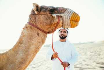 Man wearing traditional clothes, taking a camel out on the desert sand, in Dubai