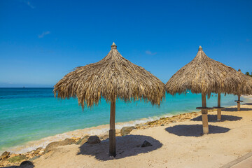 Fototapeta na wymiar View of sun beds and umbrellas on sandy beach on turquoise water surface and blue sky background. Aruba. 