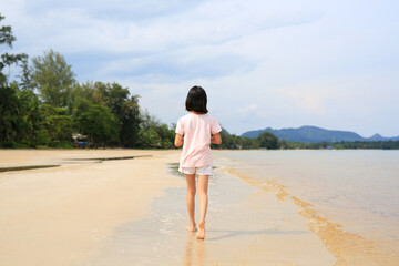 Back view of Asian girl child walking alone on tropical sand beach.