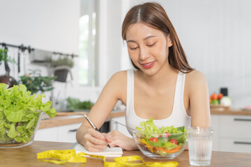Obraz na płótnie Canvas Diet, Dieting asian young woman working, write diet plan right nutrition, vegetables salad is food for good health not choose eat junk food. Nutritionist female, Weight loss person.