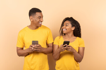 Happy african american spouses using cellphones, networking or chatting with friends, looking at each other