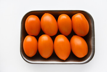 Orange ripe tomatoes on a plastic backing. Delicious tomatoes in a package from the store on a white background. Yellow tomatoes close-up. Oblong yellow tomatoes.