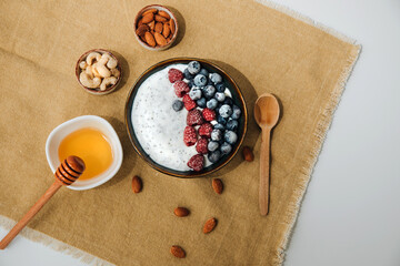 Yoghurt in green plate with blueberries, raspberries and chia seeds on the white table lined with a beige tablecloth. The concept of healthy eating. Front view
