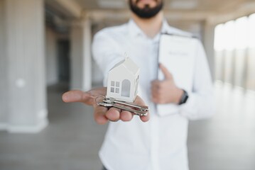Indoor portrait of happy male home owner showing key to his new house. Joyful handsome single young...