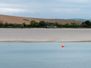 View of Clonakilty Bay at low tide. A small orange buoy is kept on a calm water surface. The sandy shore of the sea bay. The coastline on a cloudy day. Seaside landscape.