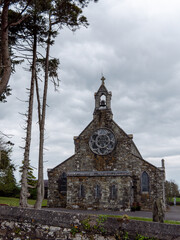 Fototapeta premium Stone Catholic Church on a cloudy day. A Christian religious building, church near trees under clouds.