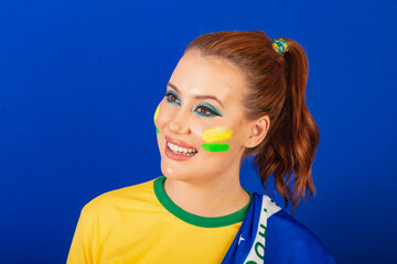 Caucasian woman, redhead, soccer fan from Brazil, Brazilian, blue background, closeup smiling with...
