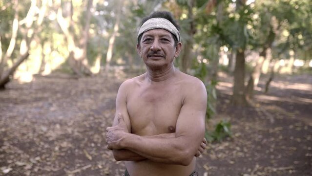 A native mayan adult man is posing shirtless wearing a paliacate in the jungle