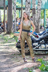 A beautiful young woman is standing next to a motorcycle. girl in a golden suit