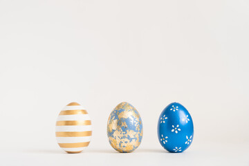 Three Easter golden decorated eggs on white background. Minimal easter concept. Happy Easter card with copy space for text. Top view, flatlay.