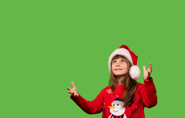 A girl in a Santa hat looks up and catches gifts or discounts with her hands. Merry Christmas and Happy New Year. Isolated on green background