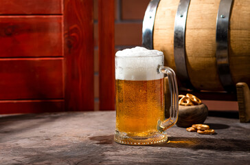 A glass of light beer on a dark table with an oak barrel next to it